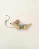 A handmade pull-along dog toy made from sustainably harvested birch wood, in the shape of a dachshund with round wheels, adorned with a green and blue plaid pattern, and a gray