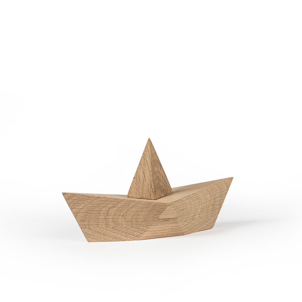 A Boyhood Admiral, Large Oak paper boat toy on a white surface with rugged, cloud-like white cutouts in the background, suggesting a minimalist artistic scene.