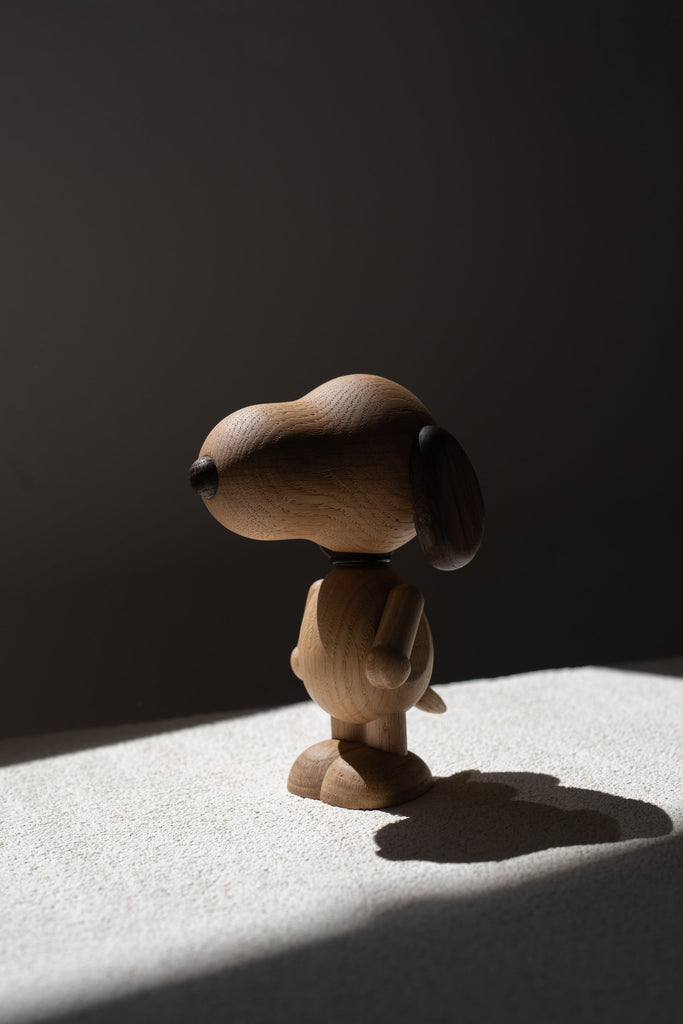 A Boyhood Snoopy, Small figurine of a beagle, with a smooth finish and oversized head, standing in a beam of sunlight casting a sharp shadow on a textured surface.