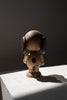 A wooden figurine of Boyhood Snoopy, small with oversized headphones stands on a stone surface, dramatically lit by natural light casting strong shadows.
