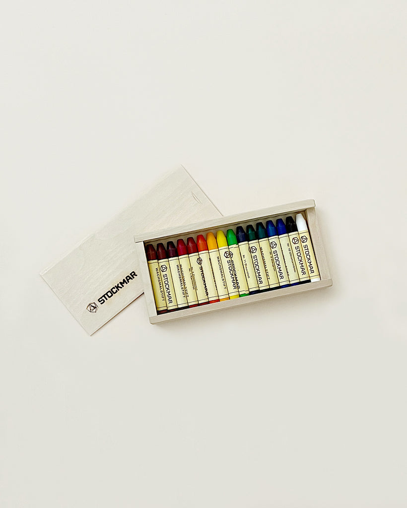 A set of non-toxic Stockmar wax stick crayons in various colors neatly arranged in an open cardboard box on a white background.