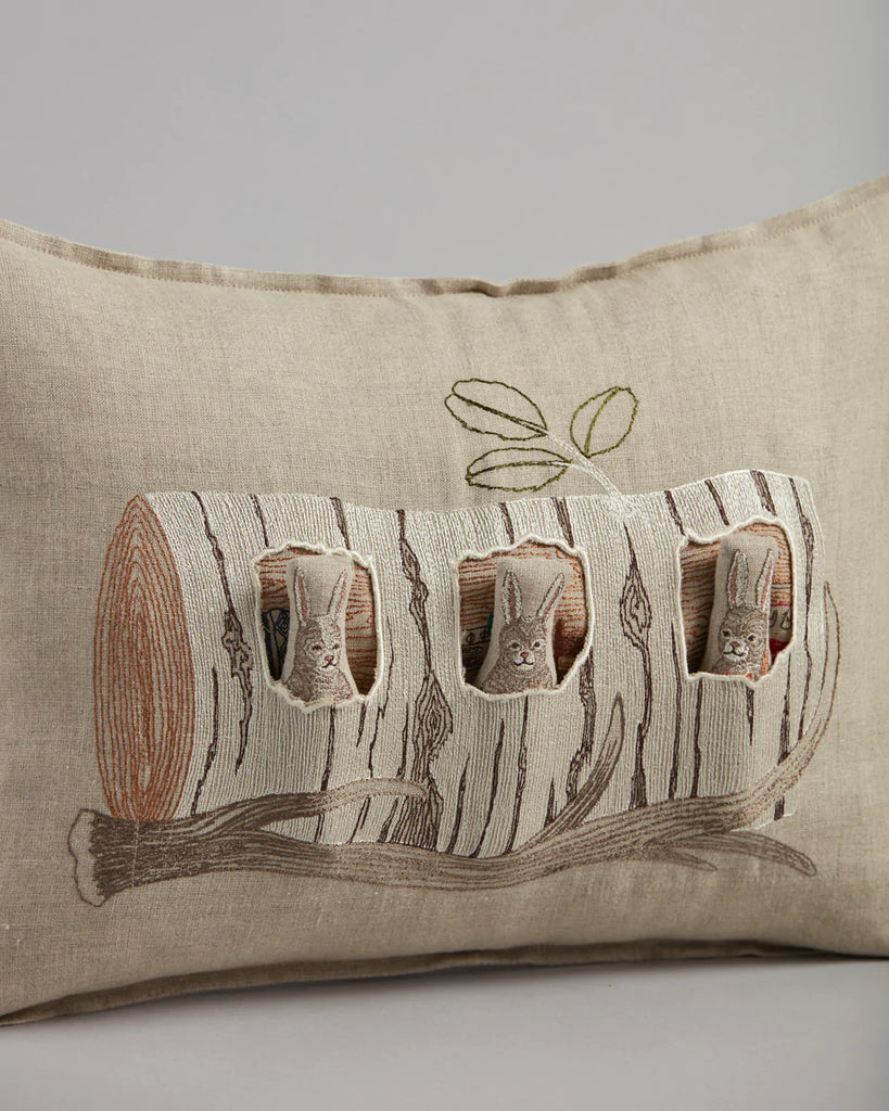 Rectangular Coral & Tusk Aspen Log Bunnies pocket pillow with a textured design featuring an embroidered log with three peeking rabbits. Neutral tones with subtle green accents on an Oeko-Tex certified embroidered linen background.