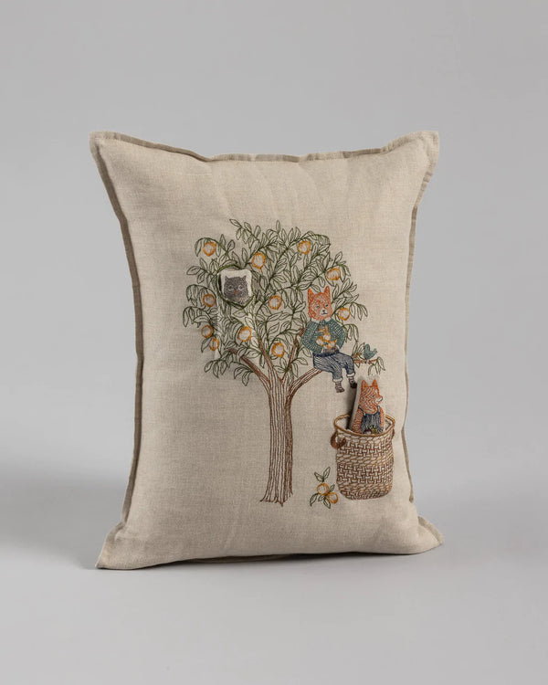 A Coral & Tusk Peach Tree pocket pillow featuring an embroidered design of a tree with two cats, one climbing its trunk and another sitting inside a basket at the base, set against a plain gray background.