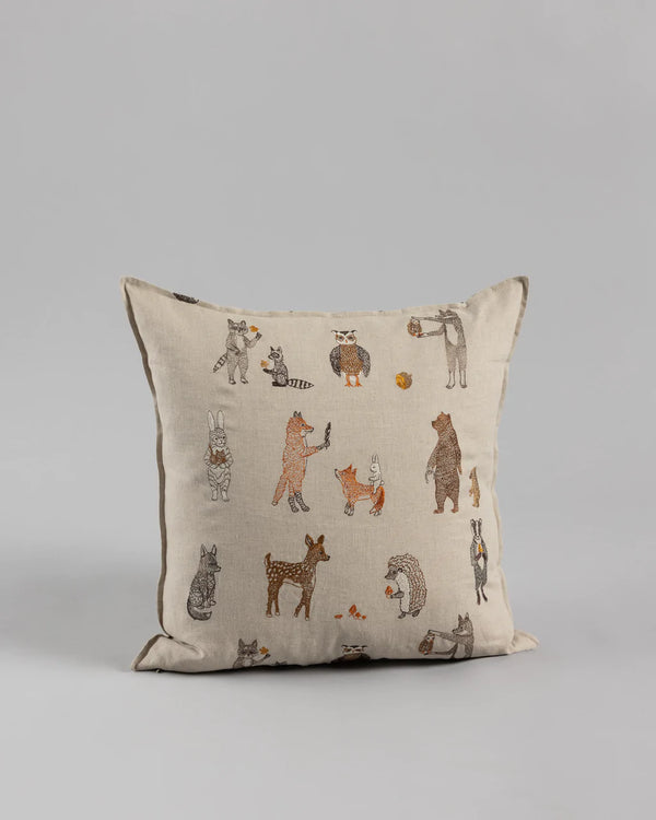 A Coral & Tusk Woodland Friends Pillow with a beige background featuring various animals dressed in human clothing, such as a fox in a suit and a foraging chipmunk with a hat, illustrated in a whimsical style