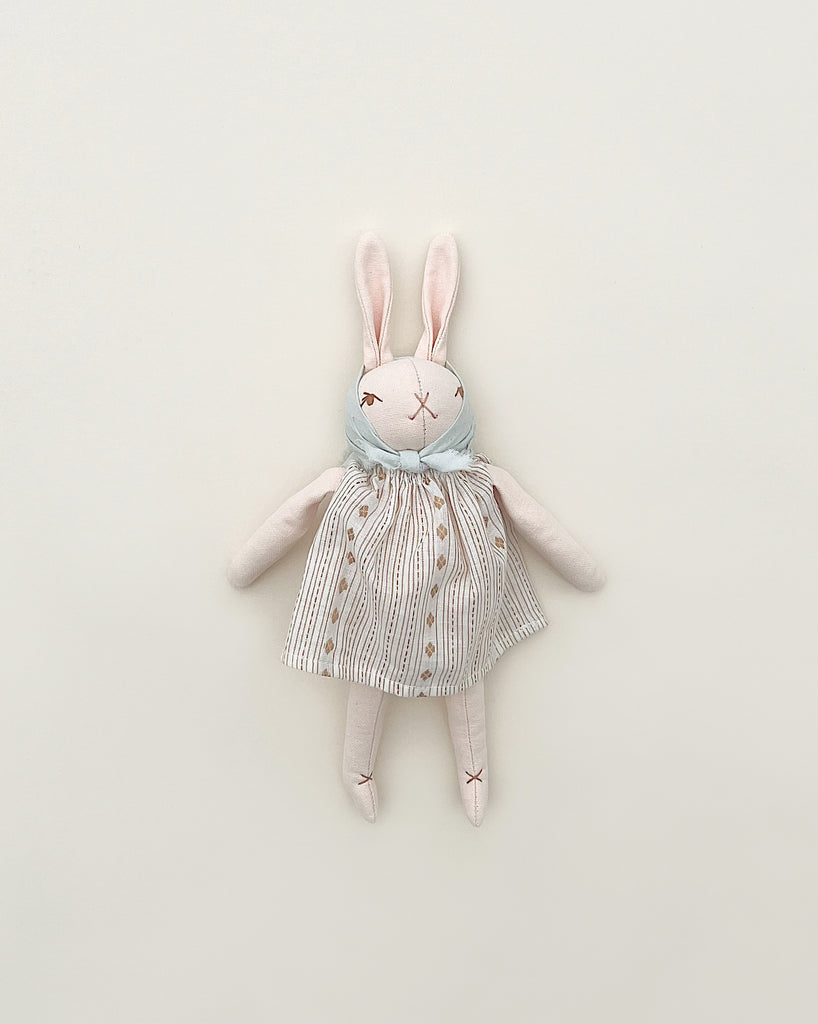 A Polka Dot Club Little Rabbit in Headscarf and Dress toy with a striped dress and a hand embroidered blue scarf, lying flat on a plain light background. The rabbit has stitched eyes and mouth, giving it a crafted look.