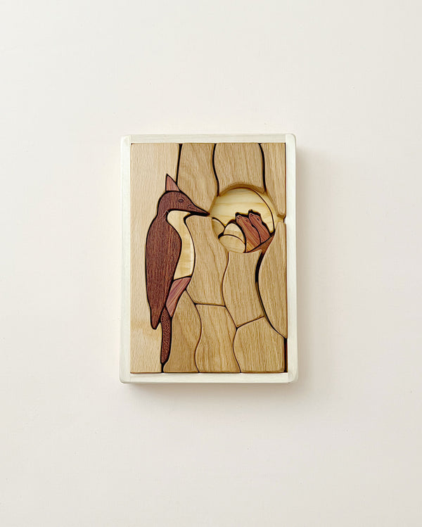 A Handmade Double Layer Wooden Puzzle - The Nest depicting a bird perched on a branch in its nesting habitat, intricately carved with natural wood grains and various shades, set against a plain off-white background.
