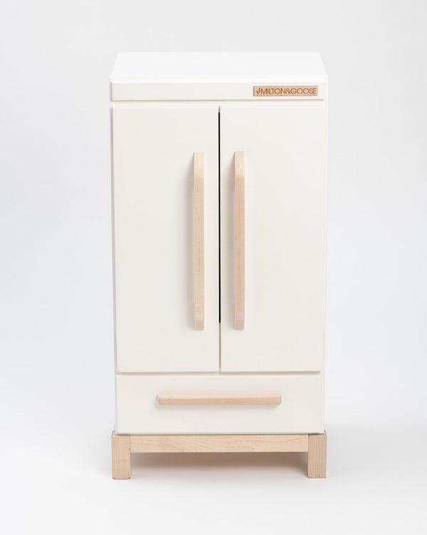 A modern white refrigerator branded as "Milton & Goose Pretend Refrigerator - Made in USA" on its top front panel, featuring wooden handles on the doors and a matching wooden base.