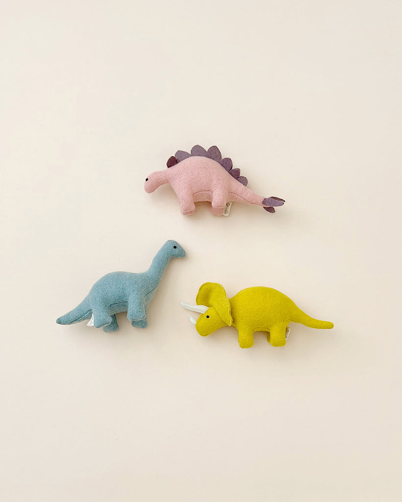 three stuffed dinosaur toys laying on a flat surface.