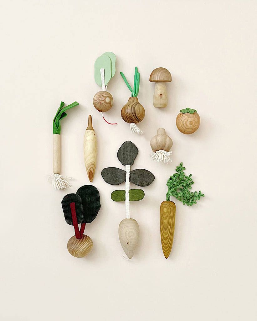 A collection of the 10 Piece Handmade Wooden Vegetable Set displayed against a light background, including a carrot, radishes, mushrooms, onions, and others with distinct, natural wood textures and colors.