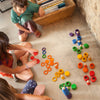Two children play with Grapat 36 Rings in 6 Colors on a tiled floor, focusing intently on arranging them into patterns. A bookshelf nearby adds a cozy element to the setting.