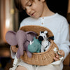 A young child gently holds a wicker basket containing three Olli Ella Holdie Folk Felt Safari Animals: an elephant, a whale, and a cow, with a soft smile on their face.