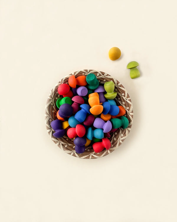 A top-down view of a basket filled with colorful Grapat Mandala Rainbow Mushrooms made from wood sourced from sustainable forests, on a light background, with some pieces scattered around it.