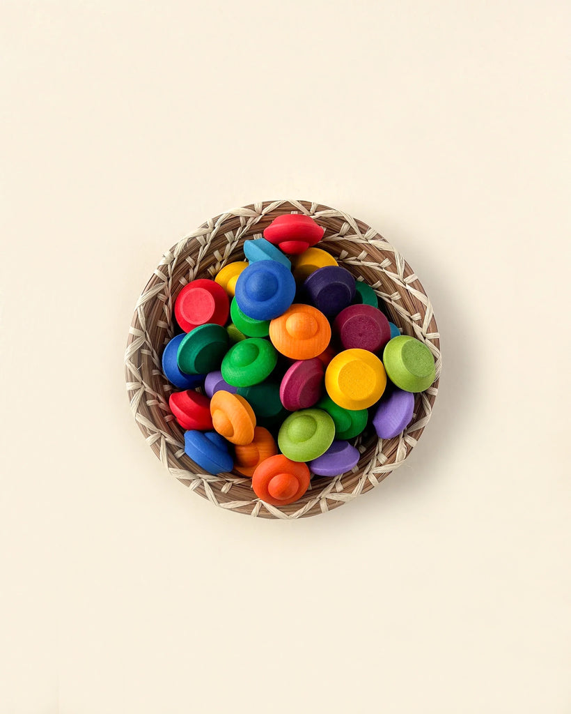 A wicker basket filled with colorful wooden toy pieces, including Grapat Mandala Rainbow Flowers and wheels, arranged neatly against a light beige background.