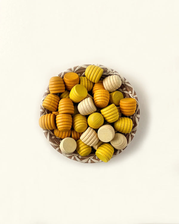 A Grapat Mandala Honeycomb containing colorful wooden beads from sustainable forests in shades of yellow and natural wood tones, viewed from above on a white background.