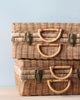 Two stacked Rattan Toaty Trunks with sturdy handles and brass clasps, set against a soft blue background.
