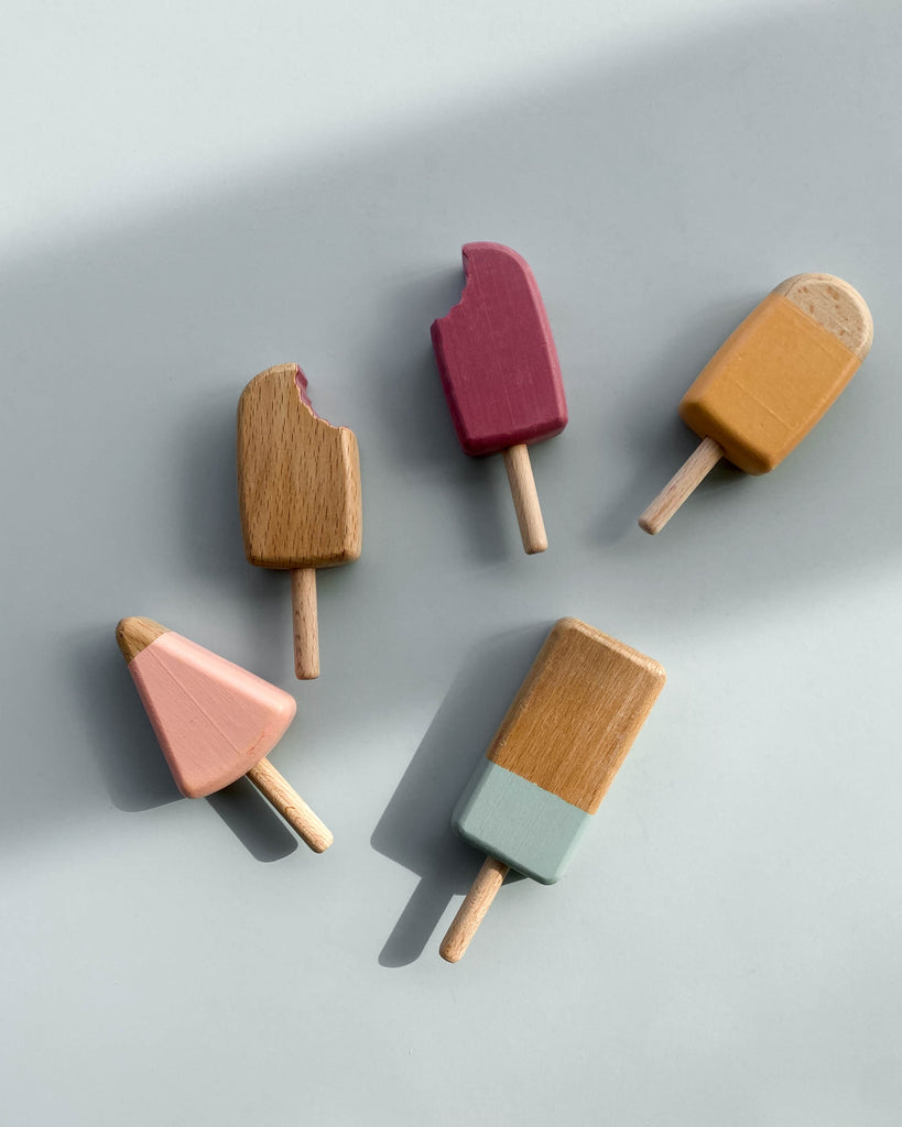 5 wooden popsicles in various popsicle shapes and in various pastel colors. Photographed laying flat.