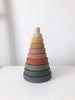 A simple photograph of a Wooden Pyramid Stacker - Green & Mustard coated in non-toxic paint, consisting of concentric rings in a gradient of warm to cool tones, set against a white background.