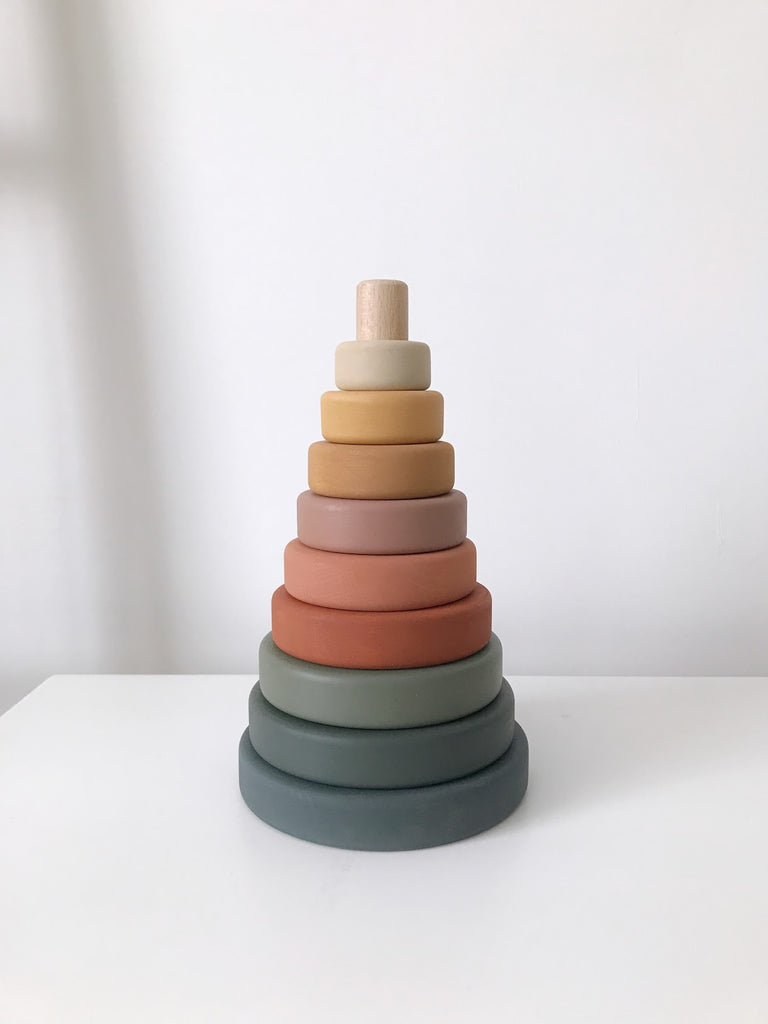 A simple photograph of a Wooden Pyramid Stacker - Green & Mustard coated in non-toxic paint, consisting of concentric rings in a gradient of warm to cool tones, set against a white background.