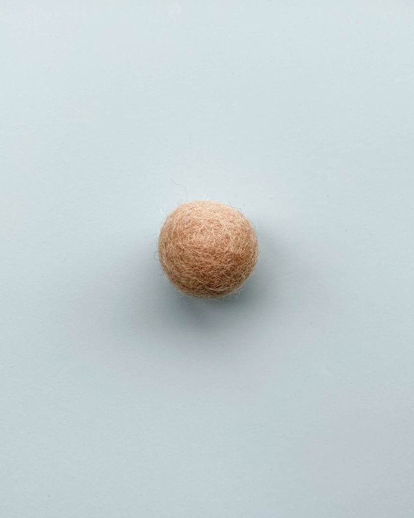 a light brown felt ball on a light blue background.