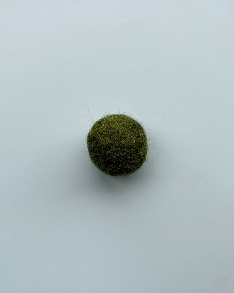 a forest green felt ball on a light blue background.