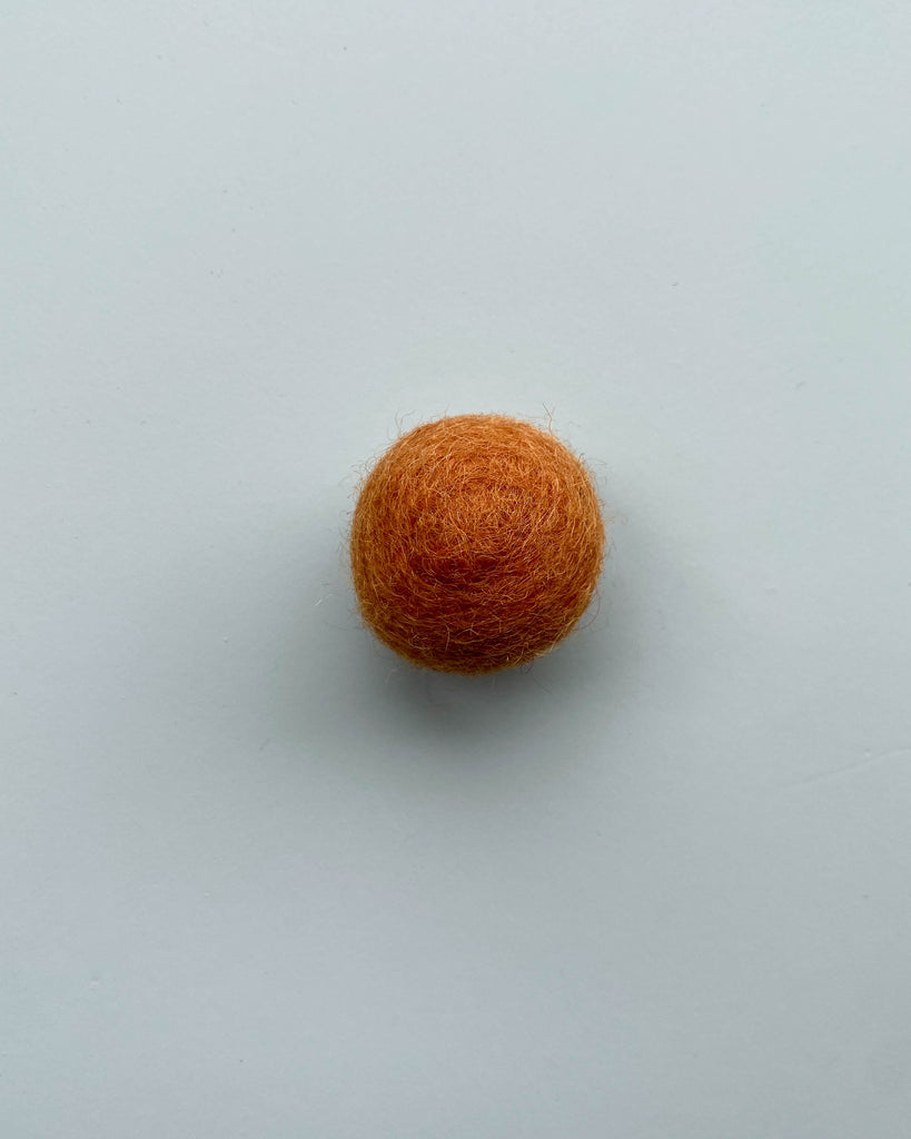 a burnt orange color felt ball on a light blue background.