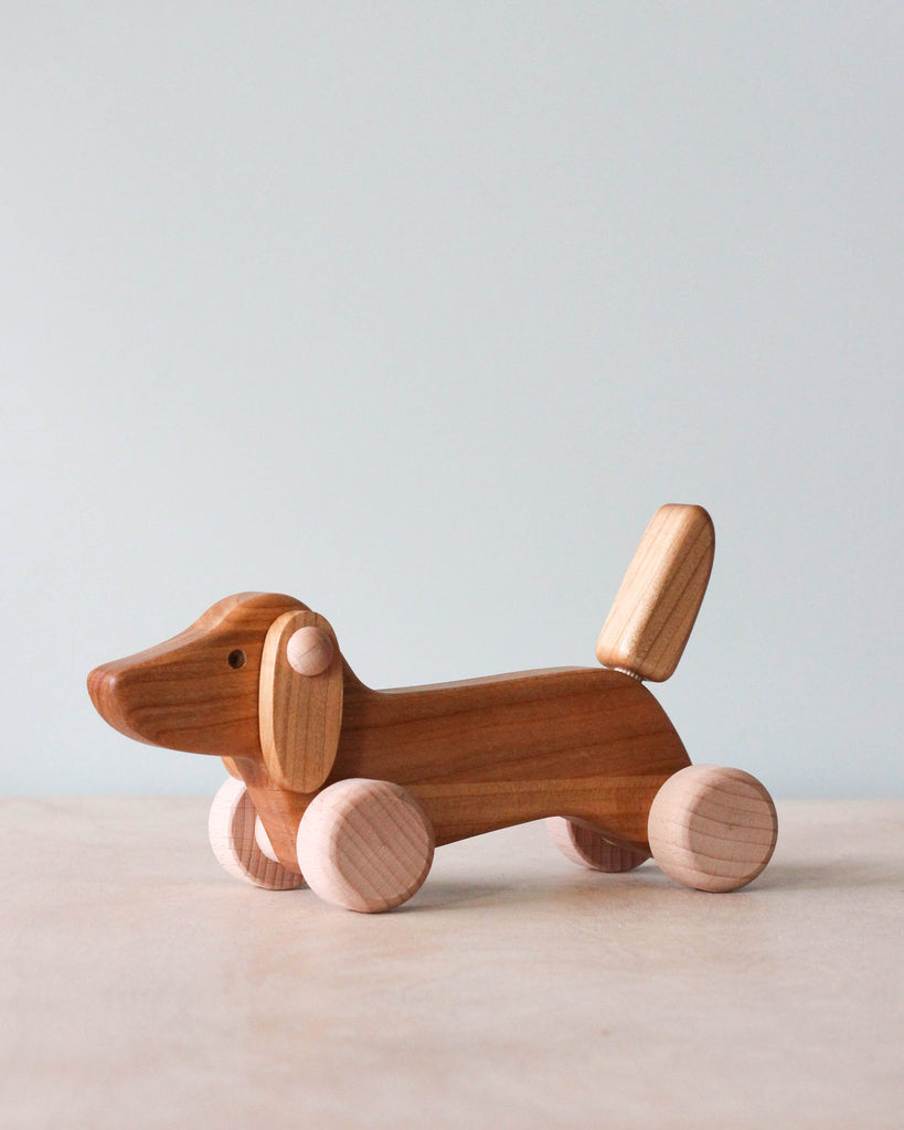 Wooden dachshund dog push toy photographed against light blue background. 