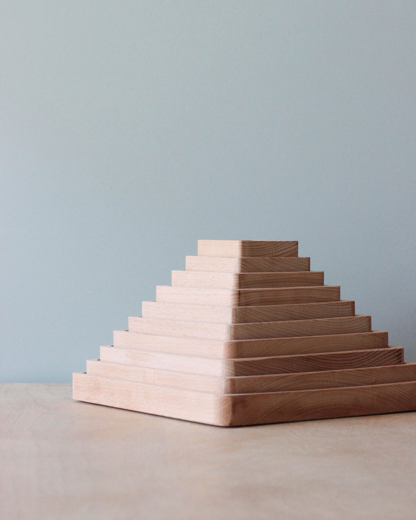 A neatly arranged stack of The Original Wooden Pyramid Counting Trays in light beech wood, set against a soft blue background. The focus is on the texture and symmetry of the blocks.