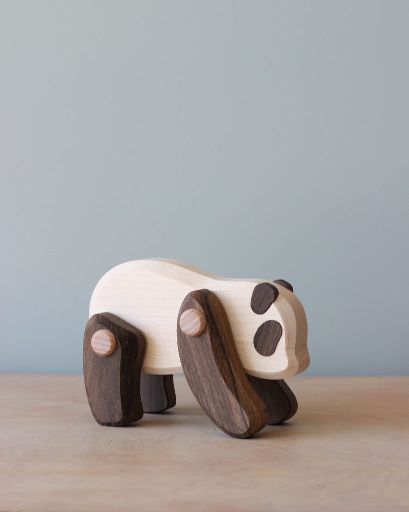 A wooden toy panda with contrasting light body and dark legs and spots, standing against a soft blue background.