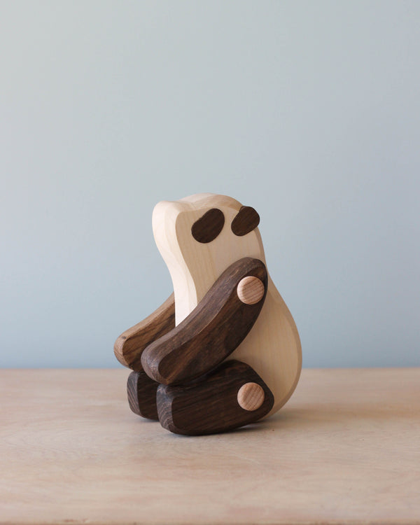 A wooden sculpture of a stylized Wooden Panda, crafted with a combination of light and dark eco-friendly woods, displayed against a soft blue background.