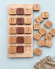 Extra Large CVC Word Kit - Made in USA educational alphabet blocks with letters carved on them, arranged on a wooden board against a light blue background. Some blocks are scattered beside the board.