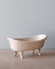 A small ceramic Maileg Mini Bathtub, positioned on a wooden surface against a light blue background.