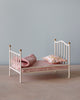 Maileg Miniature Bed with decorative golden knobs, fitted with a pink striped mattress, a floral pillow, and a matching blanket, set against a pale blue background.