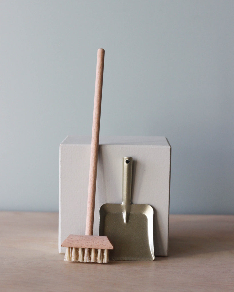 A small dustpan and Maileg | Miniature Broom Set against a plain background. The dustpan is metallic and the brush, now identified as a wooden broom, has a wooden handle; both are leaning against a simple