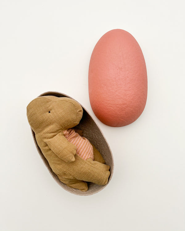 A Maileg | Medium Gantosaurus in egg - Dark Ocher tucked into the bottom half of a large, egg-shaped shell, paired with a closed, larger top shell painted in coral pink, set against a plain white background and marketed.