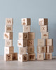 A collection of Alphabet Wooden Blocks stacked in a pyramid on a wooden surface against a blue background.