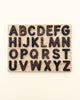 A Uppercase Walnut Alphabet Puzzle featuring all the letters of the alphabet in uppercase, carved from dark walnut wood and arranged in a five-row grid against a light background.