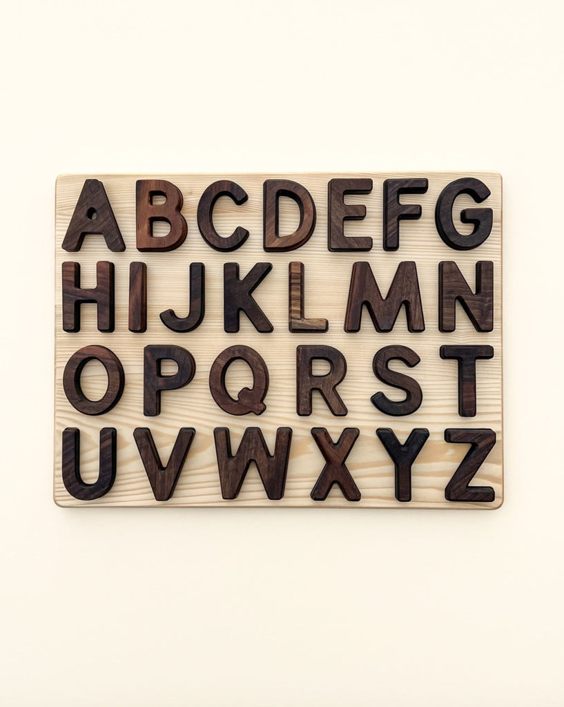 A Uppercase Walnut Alphabet Puzzle featuring all the letters of the alphabet in uppercase, carved from dark walnut wood and arranged in a five-row grid against a light background.