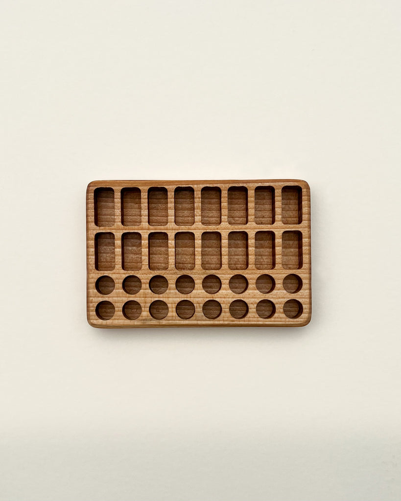 A Crayon Tray For Stockmar -16 x 16 Slots with a series of indented spaces and small circular tokens arranged in some of these spaces, photographed against a plain, light background.