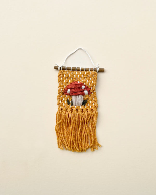 An embroidered wall hanging featuring a gnome with a white beard, red hat, and earthy tones, displayed against a neutral background.