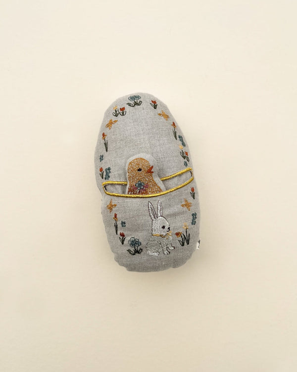 A Coral & Tusk Pocket Easter Egg with a hand-embroidered design featuring a bear, a rabbit, and floral patterns on a light background.