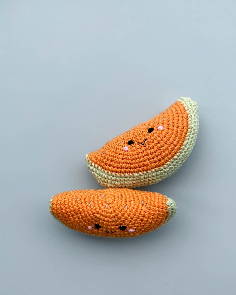 Two Handmade Melon Rattle toys with cute faces, one orange and one yellow, handmade from cotton yarn, against a light grey background.