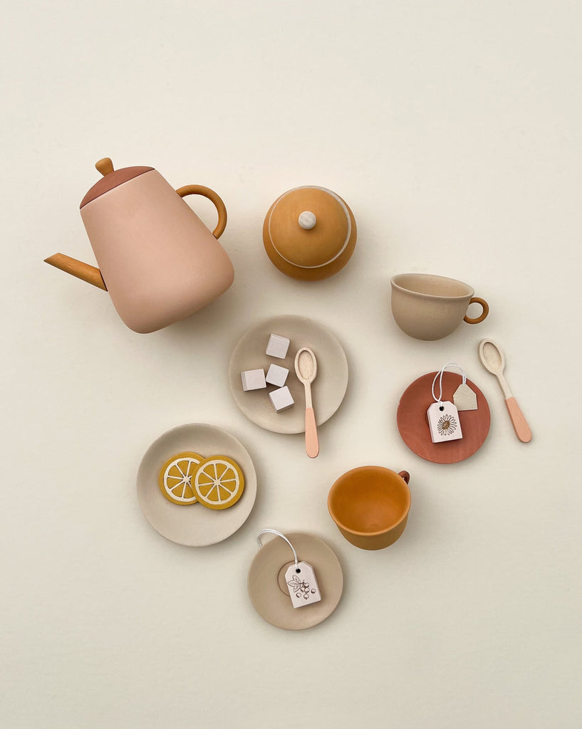 A neatly arranged Handmade Wooden Tea Set - Flower which includes a teapot, cups, saucers, and spoons, plus plates with lemon slices and sugar cubes, all in earthy tones.