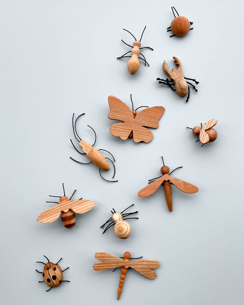 A collection of Handmade 11-Piece Wooden Insects, including butterflies, beetles, and dragonflies, artistically arranged on a plain light gray background.