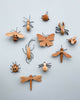 A collection of Handmade 11-Piece Wooden Insects, including butterflies, a scorpion, beetles, and a bee, artistically arranged on a pale blue background.