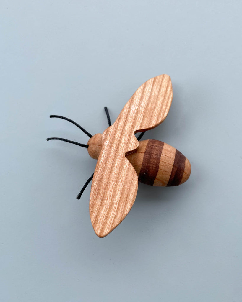 A Handmade 11-Piece Wooden Insects featuring a striped brown and beige body with black antennae, set against a light blue background.