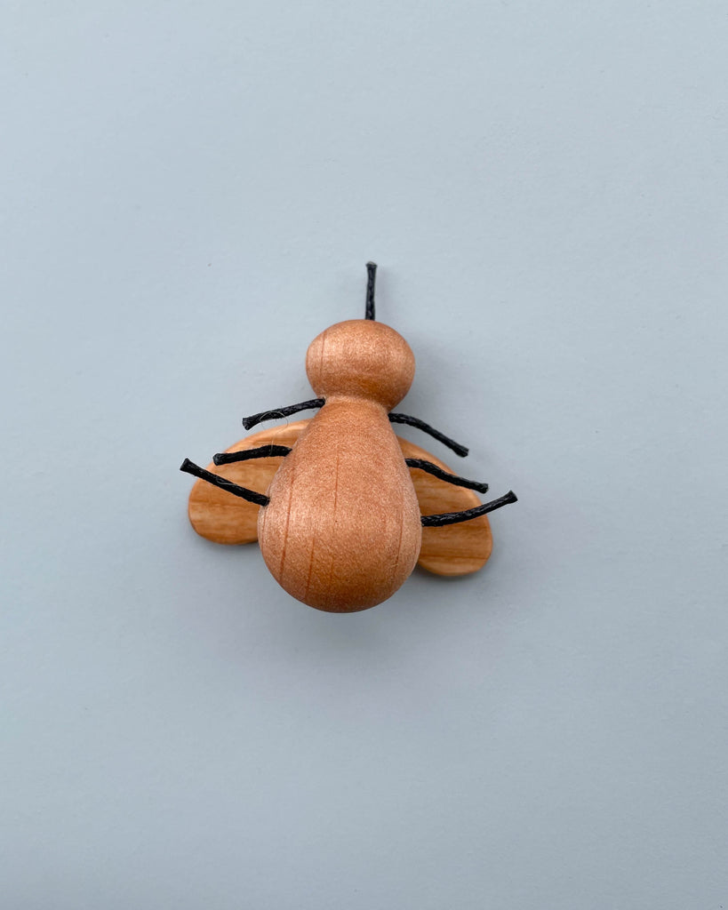 A Handmade 11-Piece Wooden Insects model with a simplified form featuring a larger round body, a smaller head, and thin wire legs, hand crafted from alder ash wood, displayed against a plain light gray background.