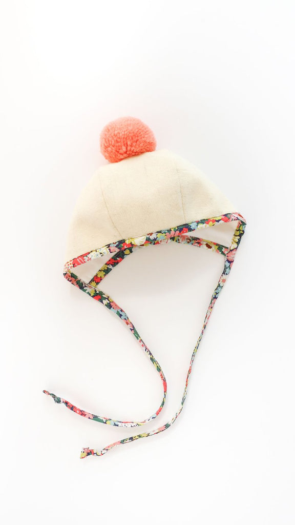 A Briar Baby Wild Poppy Pom Bonnet with Liberty of London cotton floral printed ties, isolated on a white background.