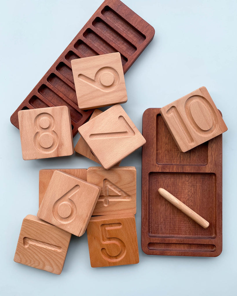 The Wooden Counting & Tracing Tray - Made in USA includes engraved number tiles (4-10), a tracing board with pen, and two wooden trays—one with slots and one with rectangular compartments—for interactive learning.