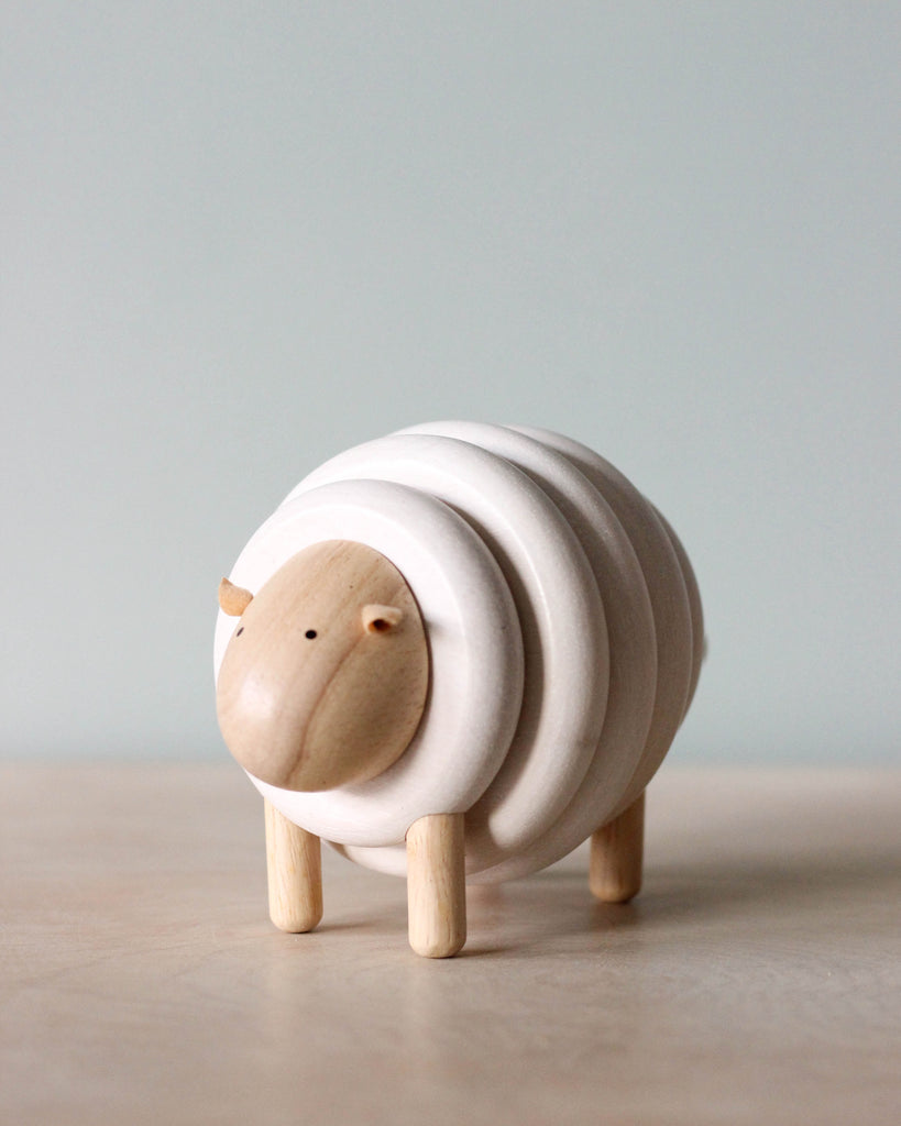 A Lacing Wooden Sheep with a simplistic design, featuring layered rings for its body and small, round head with minimal features, standing on a light surface against a soft blue background.