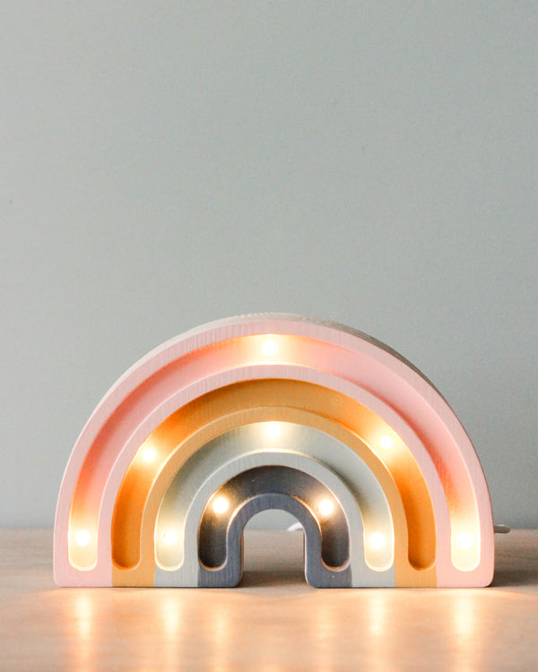A decorative handmade Little Lights Mini Rainbow Lamp with several arches illuminated from within by LED lights, set against a soft grey background. Each arch has a pastel gradient of pink to orange.